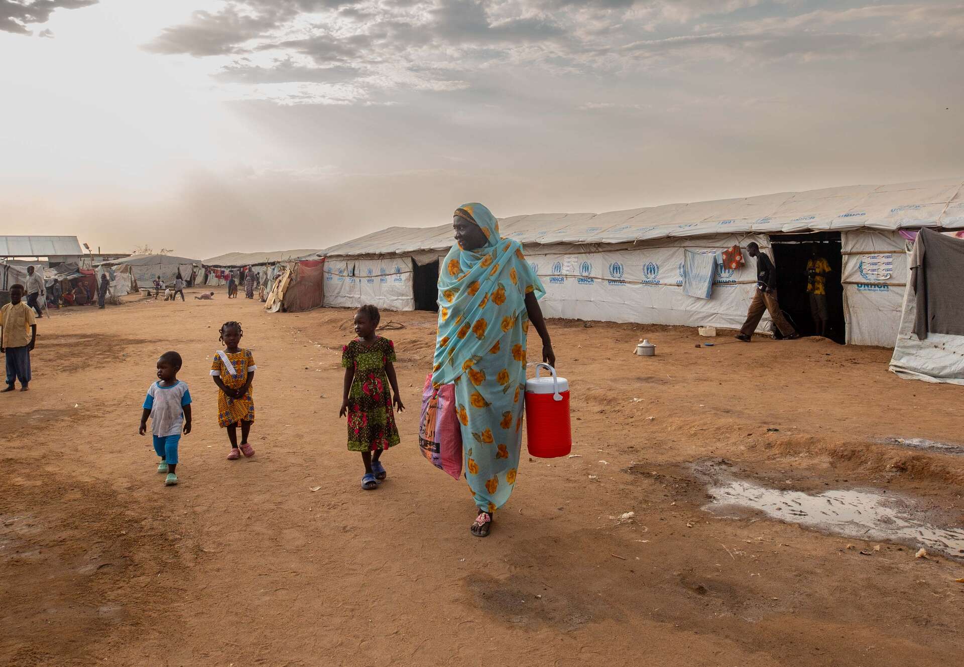A displaced Sudanese family walking through a refugee camp