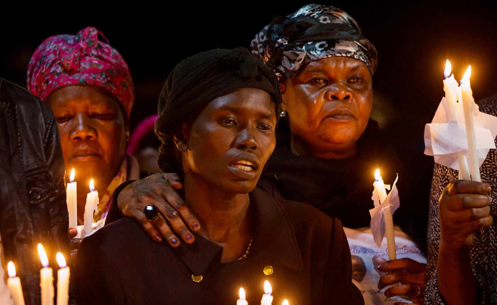 Women holding candles together at a nighttime vigil