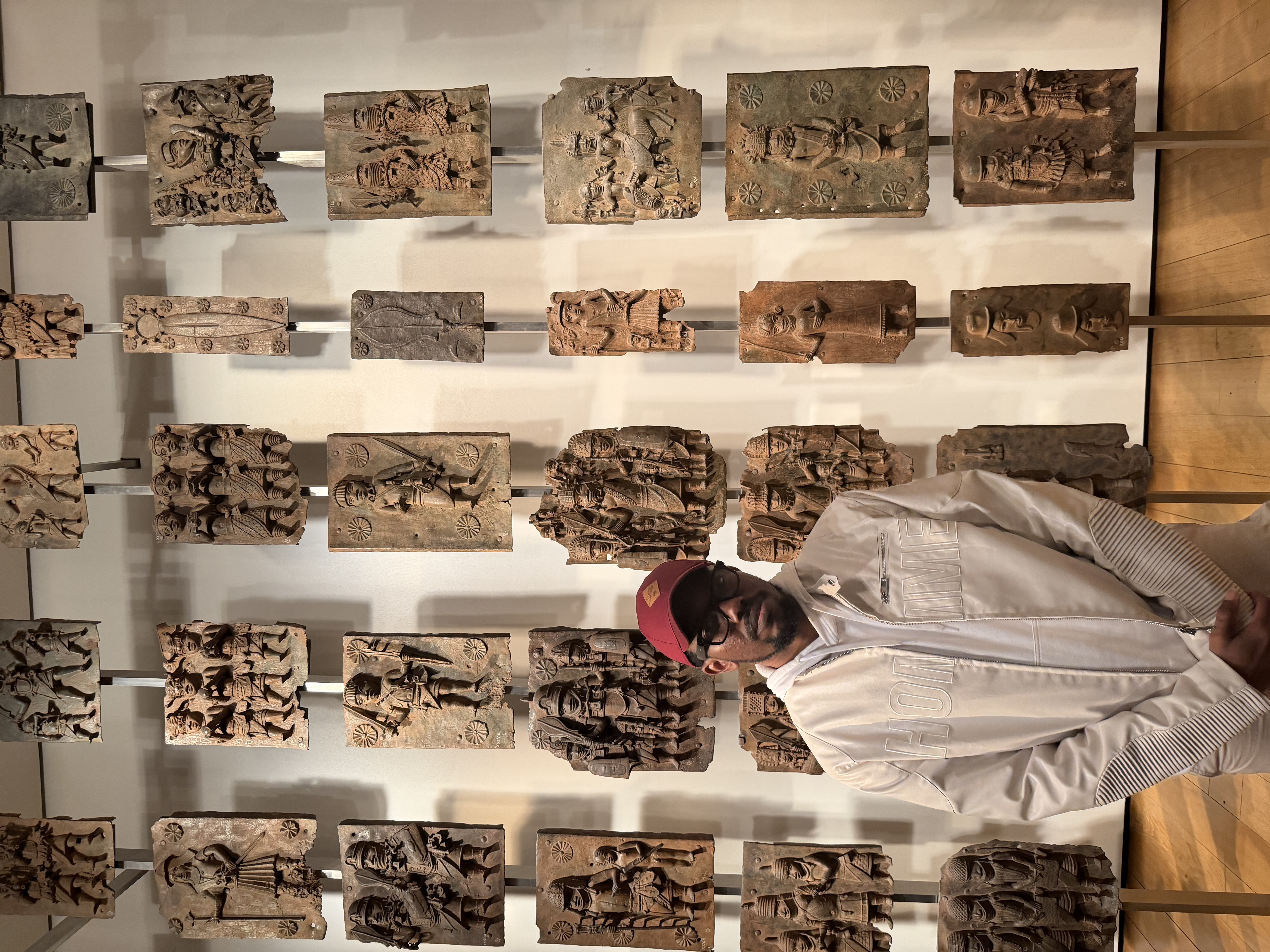 Nigerian artist Greo standing in front of historical Benin plaques