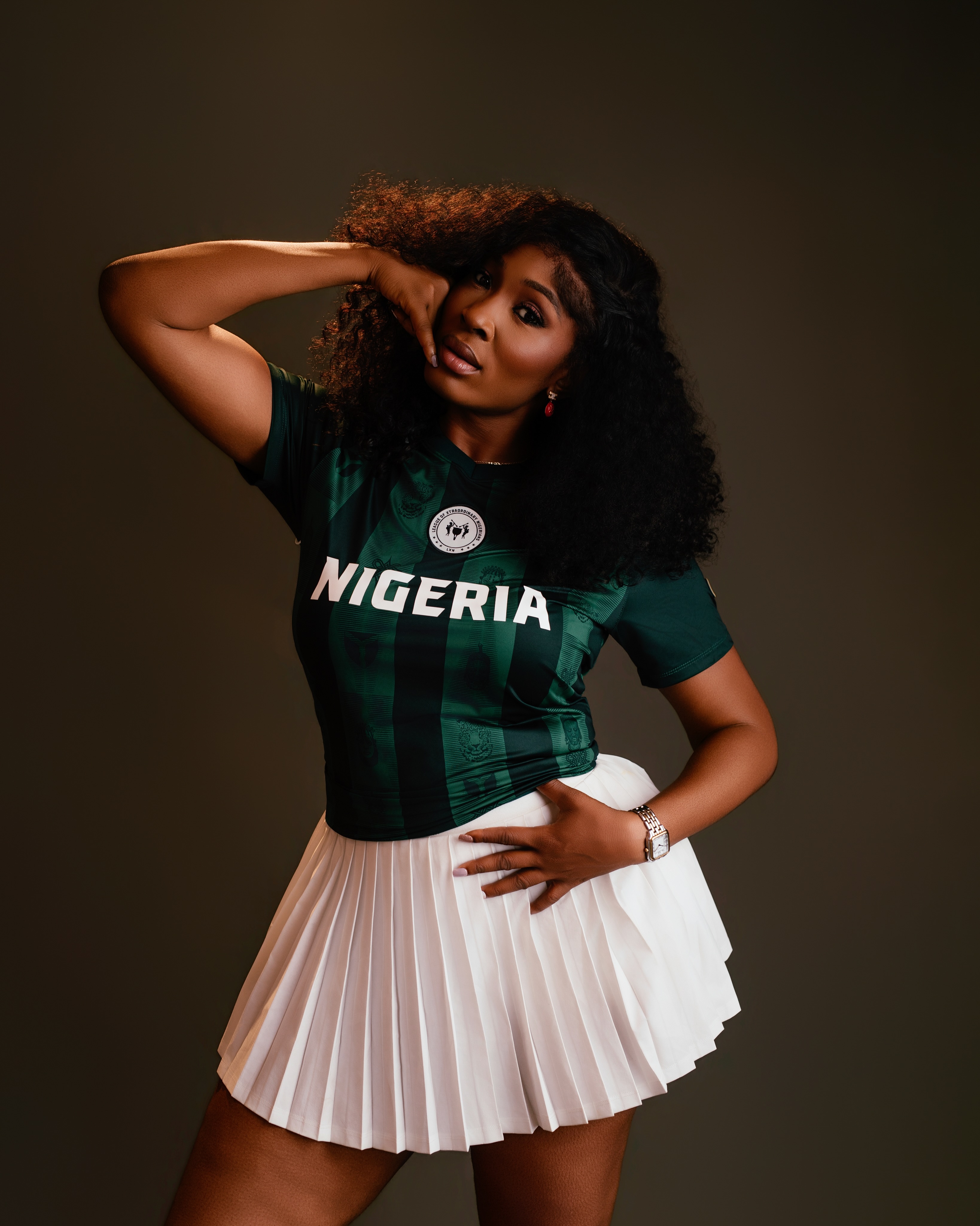 Tope Olowoniyan wearing a green Nigeria jersey and white pleated skirt in a studio portrait