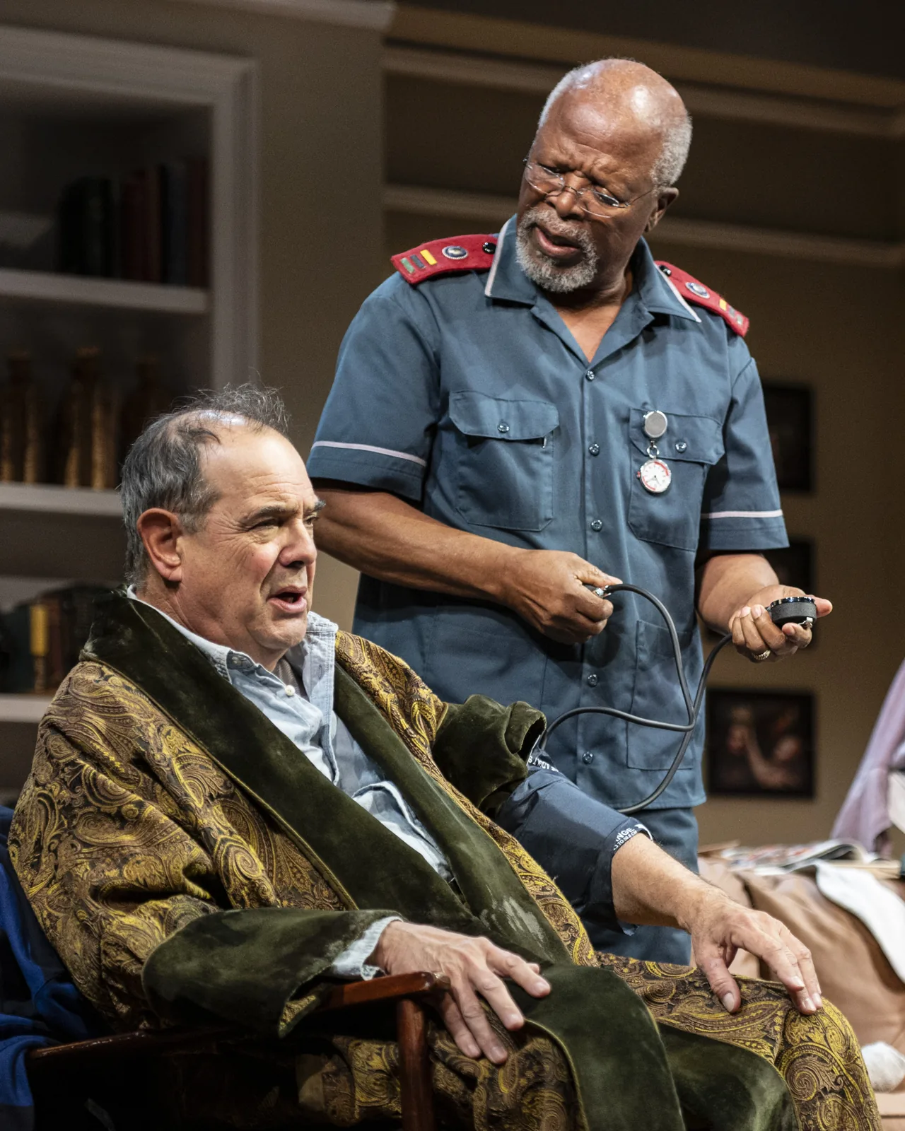 John Kani as nurse Lunga Kunene using a blood-pressure cuff beside Edward Gero as Jack Morris in a staged scene.